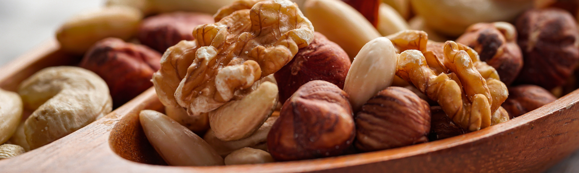 Zoomed in image of a dark wooden spoon filled with a variety of nut types.
