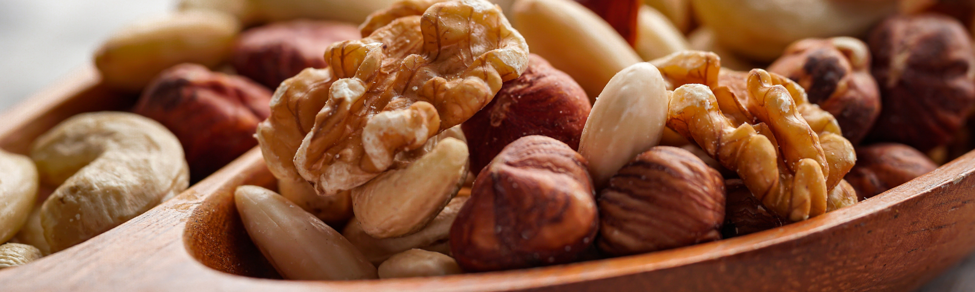 Zoomed in image of a dark wooden spoon filled with a variety of nut types. 