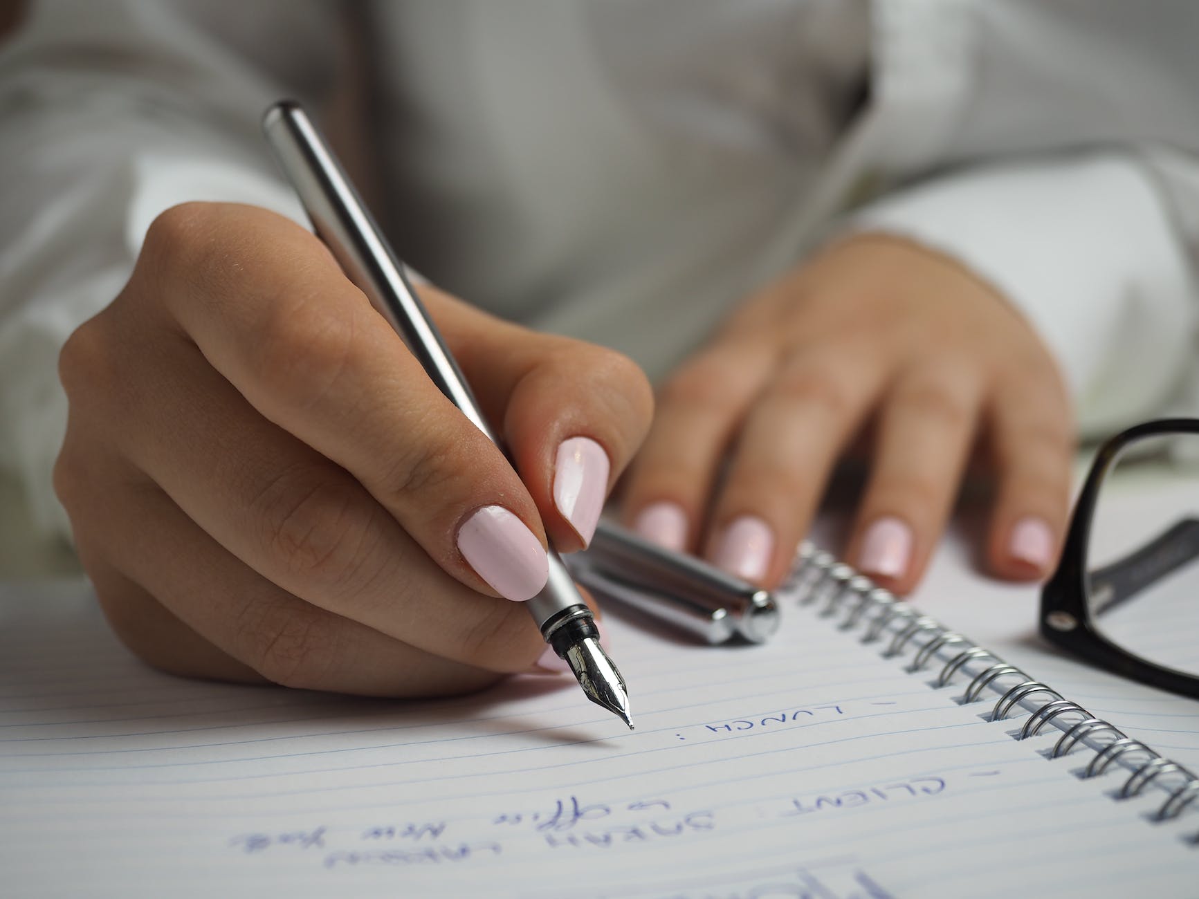 Close-up photo of someone writing in a ring bound notepad with pale pink nails. 