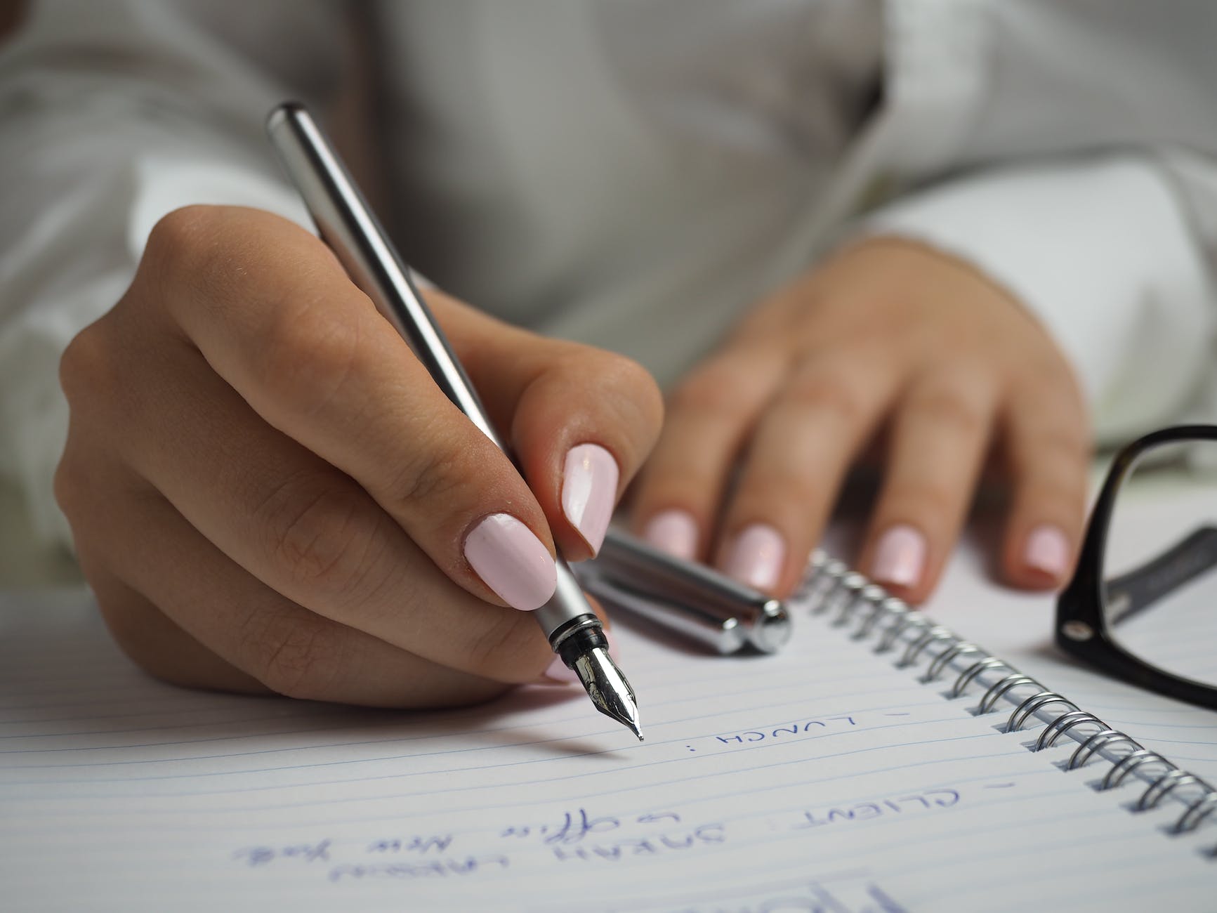 Close-up photo of someone writing in a ring bound notepad with pale pink nails.