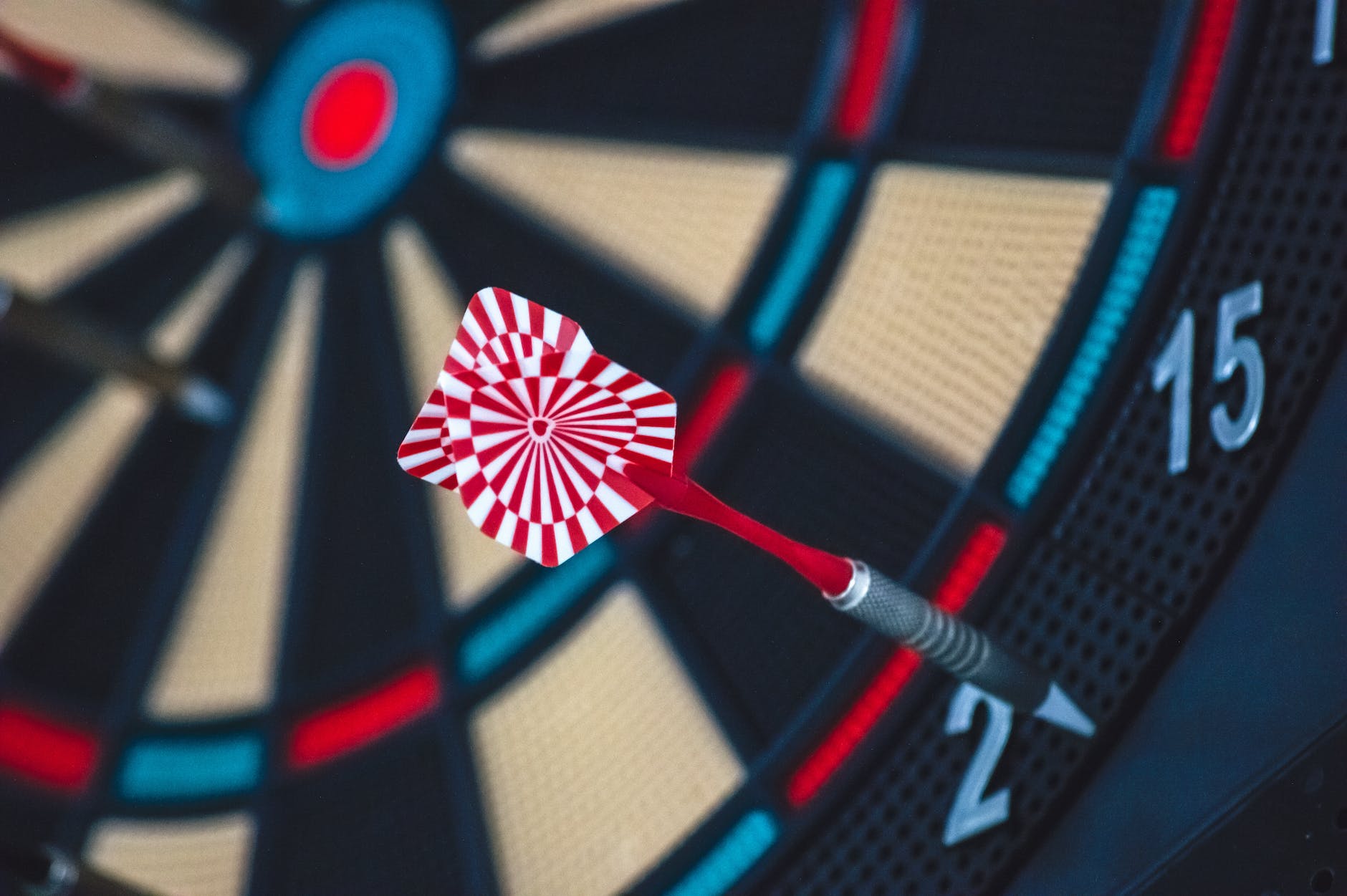 Zoomed in shot of a red and white striped dart stuck on the outskirts of a black and red dart board.