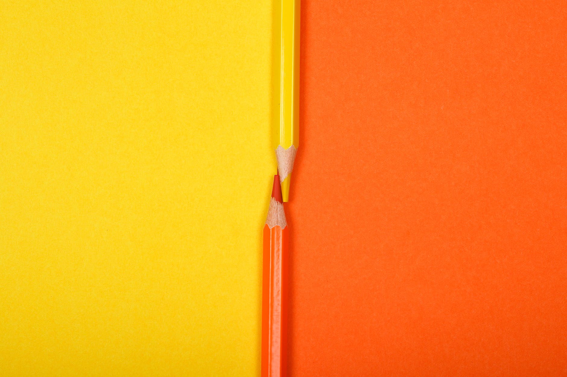 An image split vertically in half in block colours of yellow and orange with contrasting-corresponding coloured pencils aligned beside each other. 