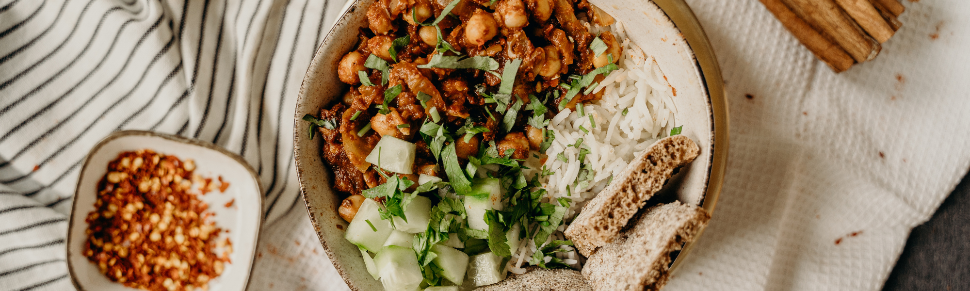 A vegan food dish served in an off-white bowl and laid on a striped white tablecloth.